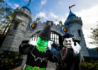 A lego green witch and a lego vampire at the gates of a castle.